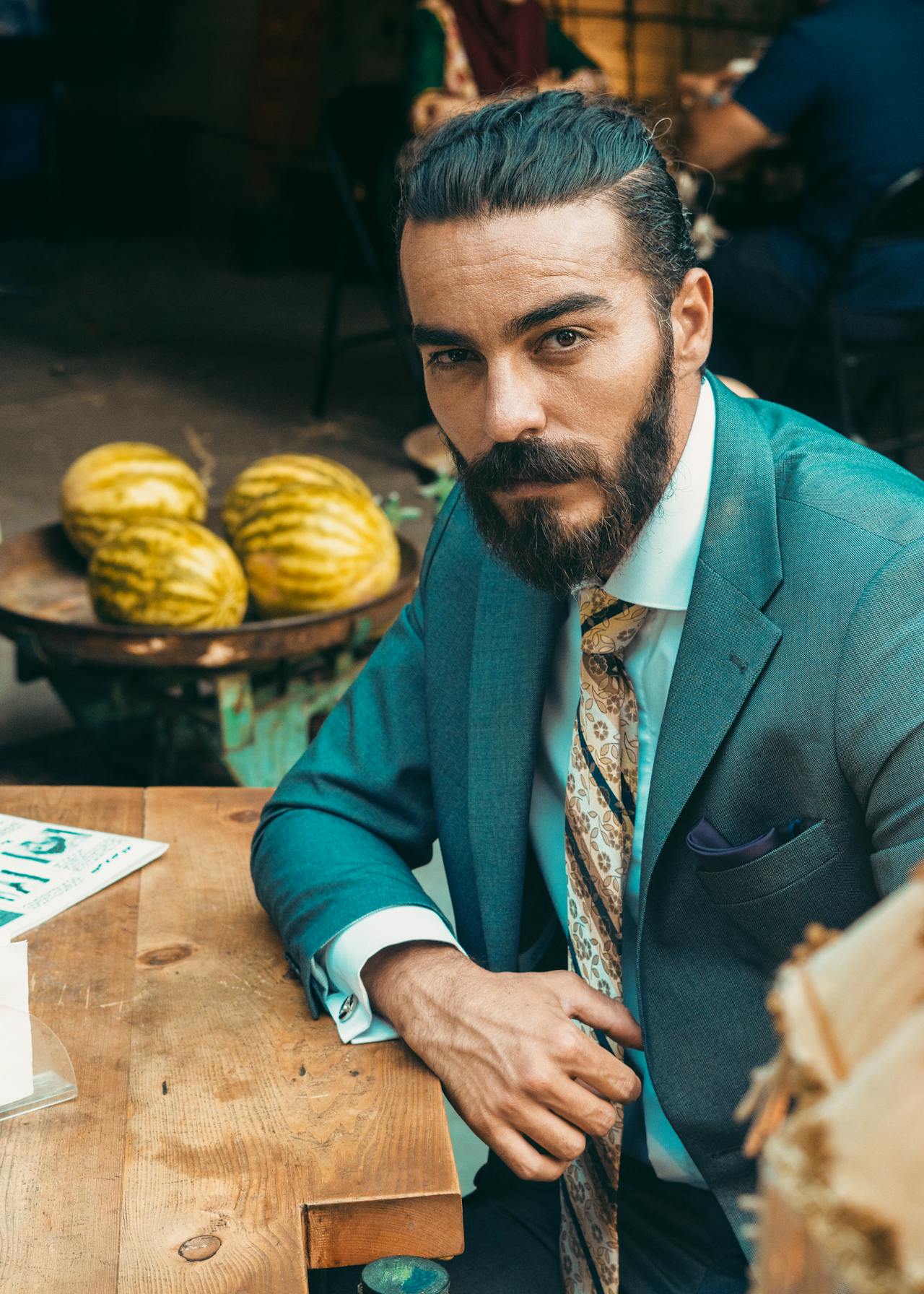 Stylish man with a neat beard and blue suit sitting confidently at a rustic table