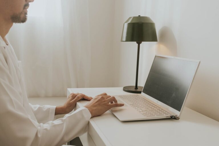 A man in a white shirt working on a laptop in a minimalist workspace, possibly searching for SEO jobs online.